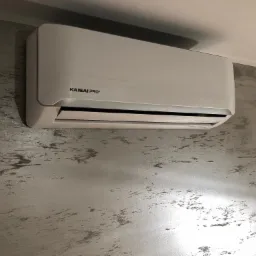 Biały klimatyzator Kaisai Pro+ zamontowany na ścianie o dekoracyjnej, srebrno-szarej fakturze.