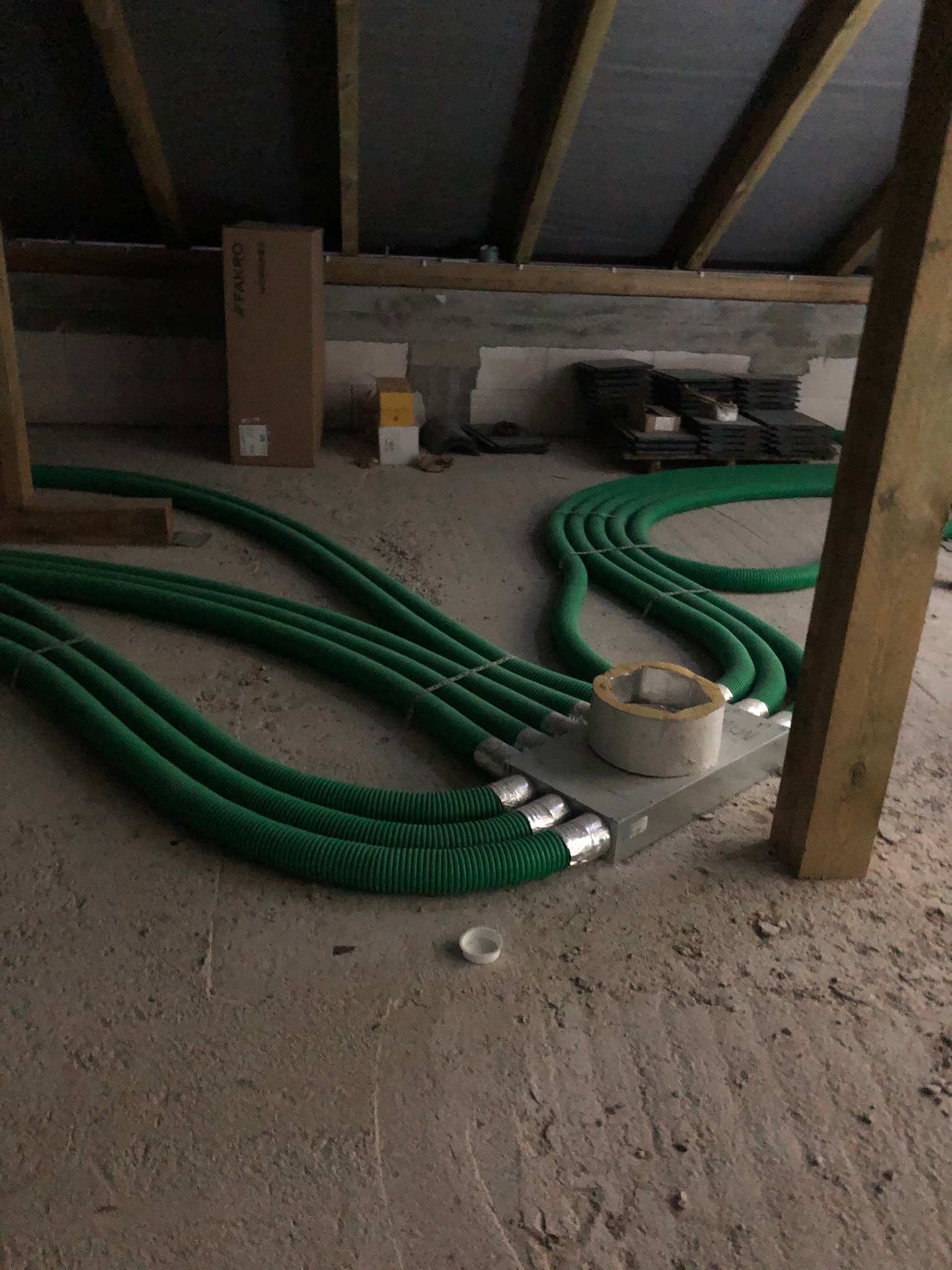 Montaż instalacji wentylacyjnej z zielonymi rurami w surowym wnętrzu poddasza, widoczna skrzynka rozdzielcza i elementy konstrukcyjne dachu.