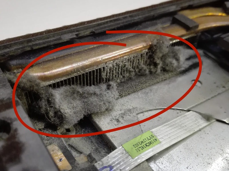 Zanieczyszczony kurzem radiator procesora wewnątrz laptopa, widoczne żeberka chłodzące zatkane kurzem, okrąg zaznaczony na czerwono.