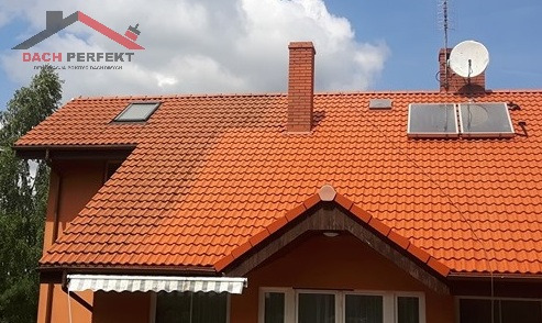 Częściowo oczyszczony, pomarańczowy dach z dachówki ceramicznej z kominem, oknem dachowym i panelami solarnymi, widoczna różnica w kolorze przed i po czyszczeniu.