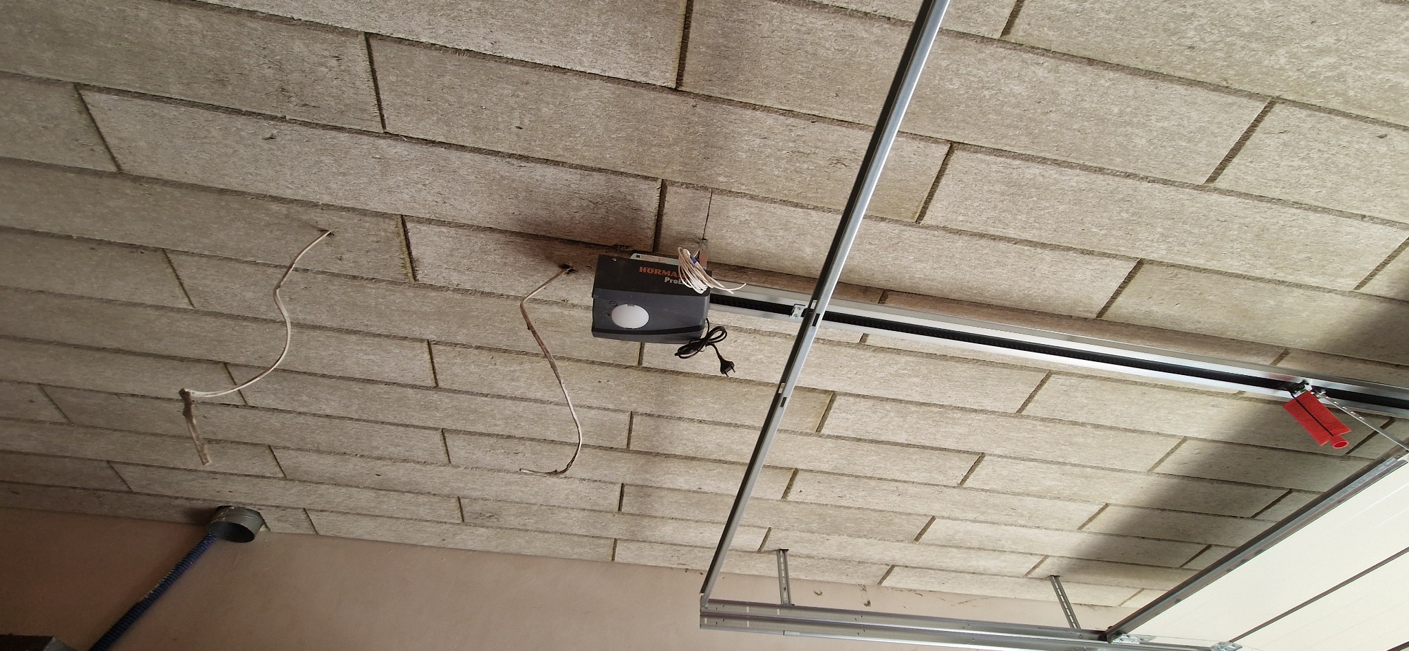 Płyty z wełny drzewnej na suficie garażu, widoczny automat do bramy garażowej Hormann Pro z przewodami i elementami konstrukcyjnymi bramy.