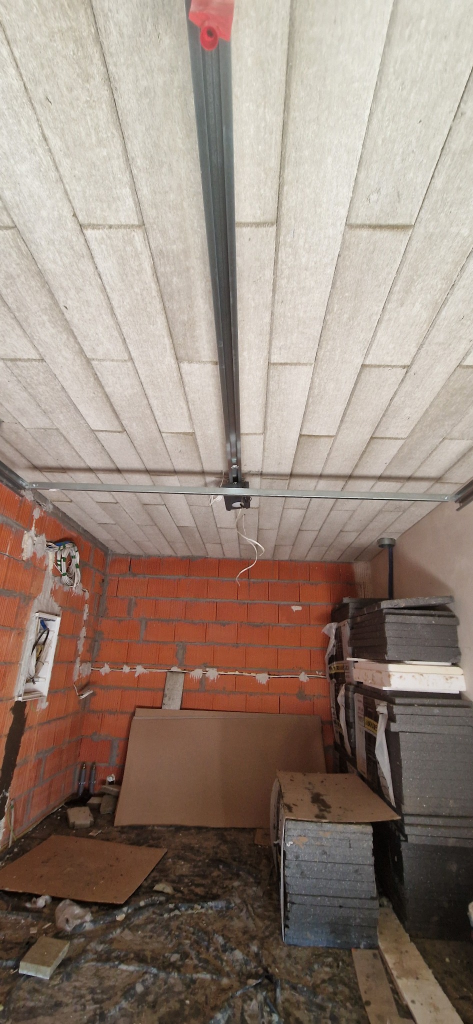 Montaż sufitu z płyt izolacyjnych w pomieszczeniu z instalacją elektryczną i elementami konstrukcyjnymi. Widoczne profile i materiały izolacyjne.