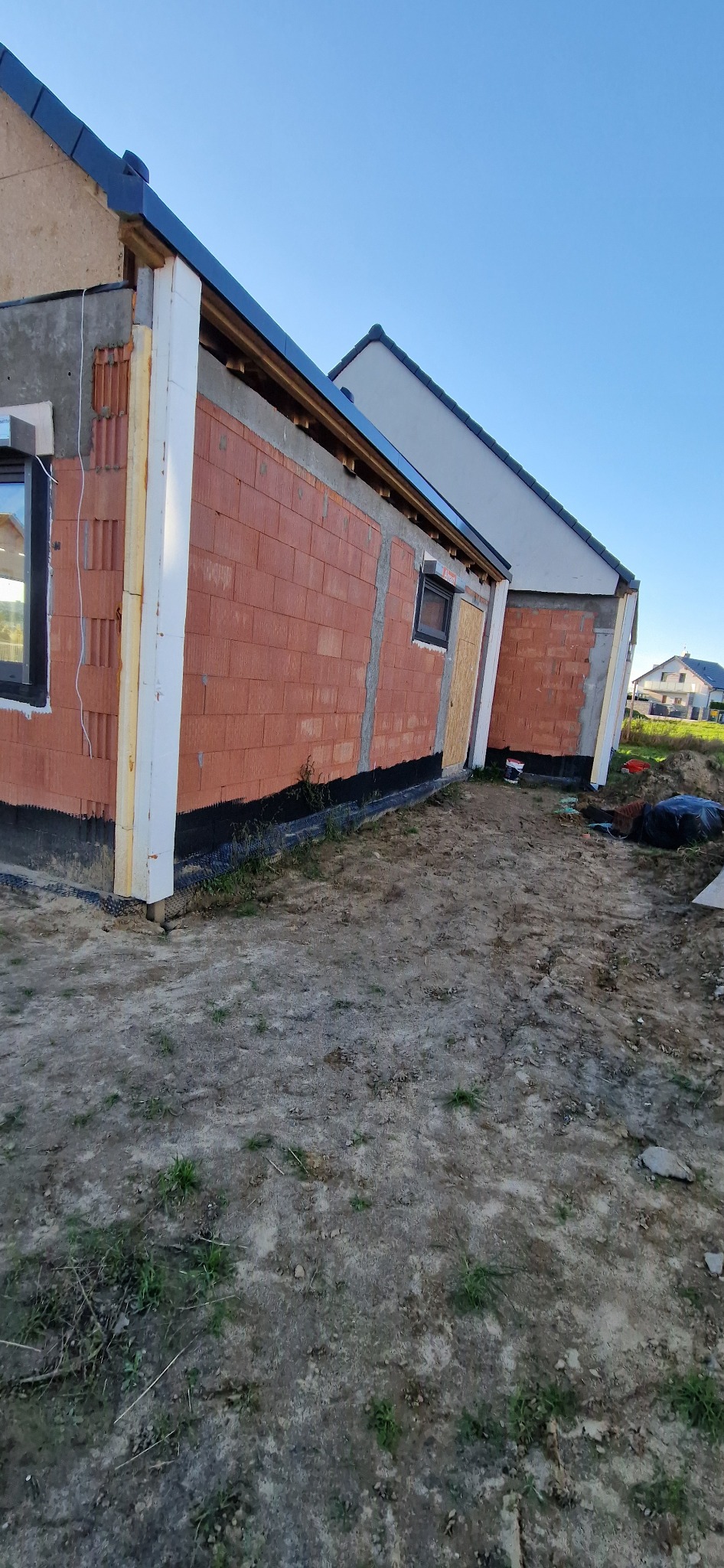 Budowa domu jednorodzinnego w trakcie ocieplania: widoczne bloczki z ceramiki poryzowanej, izolacja pionowa fundamentów i częściowo zamontowana izolacja termiczna.