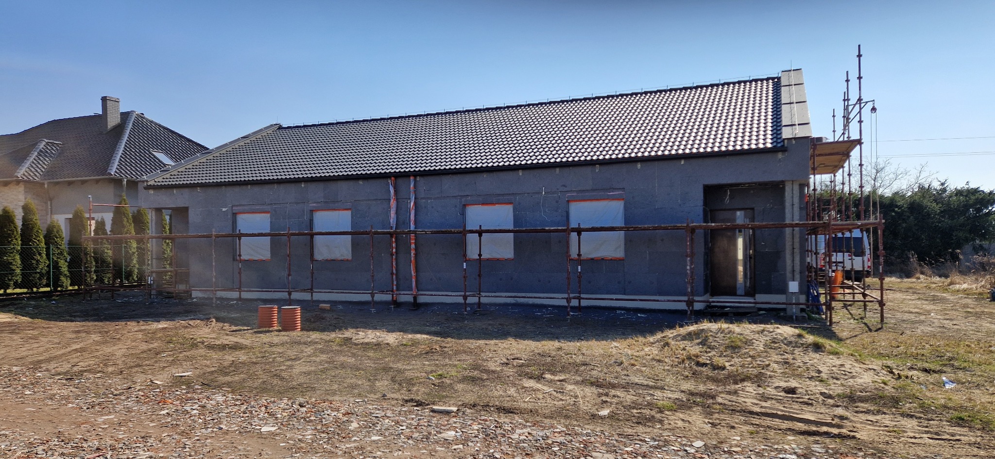 Dom w trakcie ocieplania elewacji styropianem grafitowym, z widocznymi rusztowaniami i zabezpieczonymi oknami. Dach pokryty ciemną dachówką.
