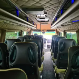 Wnętrze luksusowego busa z brązowymi skórzanymi siedzeniami, oświetleniem LED i pikowaną podsufitką. Widok na kabinę kierowcy przez przejście między rzędami siedzeń.