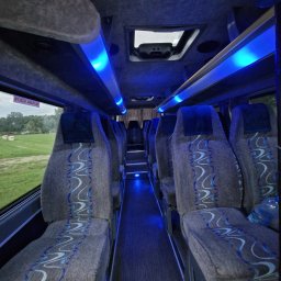 WIK - MAR MAREK WOLAŃSKI - Wnętrze autobusu z szarymi fotelami z niebieskim wzorem, podświetlonymi niebieskim światłem LED, widok z perspektywy pasażera w kierunku przodu pojazdu.