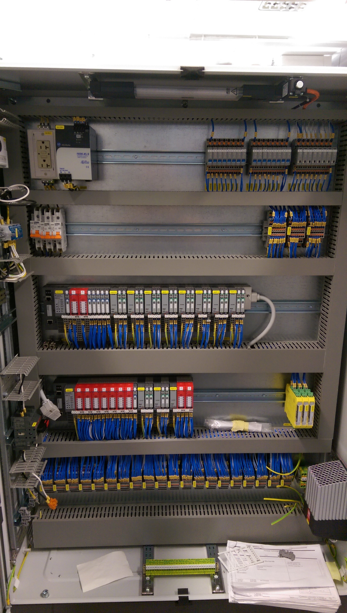 Rozdzielnica elektryczna z modułami sterującymi, okablowaniem i dokumentacją techniczną na dole.