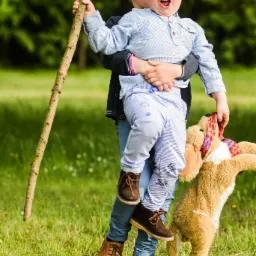 Chłopiec niesiony przez starszego brata trzymający kij i pluszowego psa na trawie.