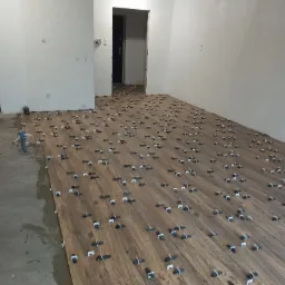 Układanie płytek imitujących drewno na podłodze w nowym mieszkaniu z użyciem klipsów poziomujących, widoczny stan surowy ścian i podłogi.