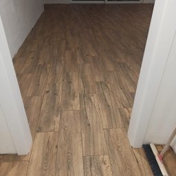 wykonczeniowka plytki regips szpachlowanie i inne - Ułożona podłoga z paneli imitujących drewno, widok z perspektywy wejścia do pomieszczenia, przy futrynie stoi zmiotka.