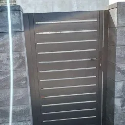 Nowoczesna, pozioma brama w kolorze antracytu, zamontowana między dwoma słupkami z szarej kostki betonowej, widoczna klamka i zamek.