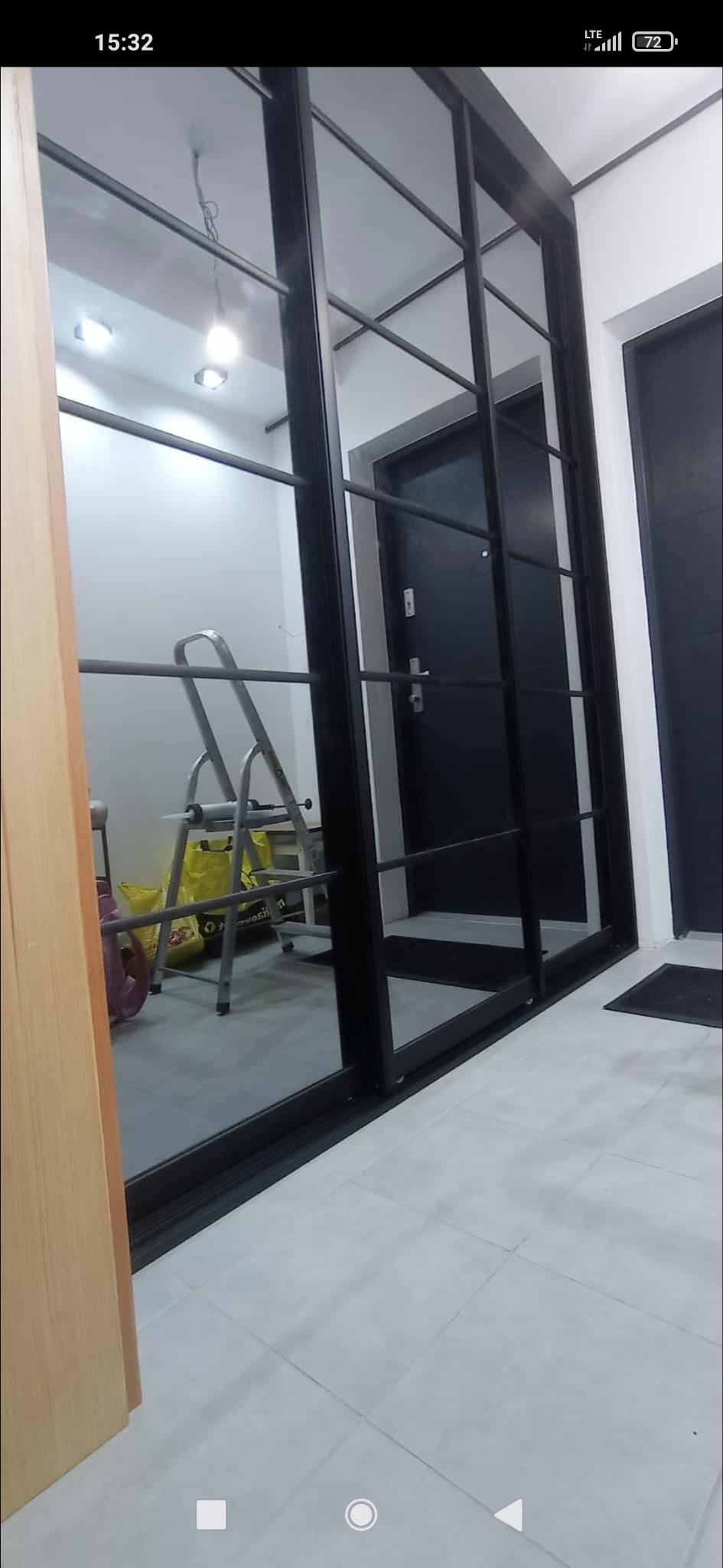 Nowoczesne drzwi przesuwne z czarnymi ramami, widoczne w korytarzu z szarą podłogą. W tle drabina i torby.