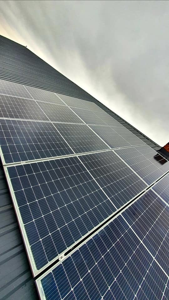 Panele słoneczne zamontowane na metalowym dachu w pochmurny dzień, widoczne z dołu pod kątem.