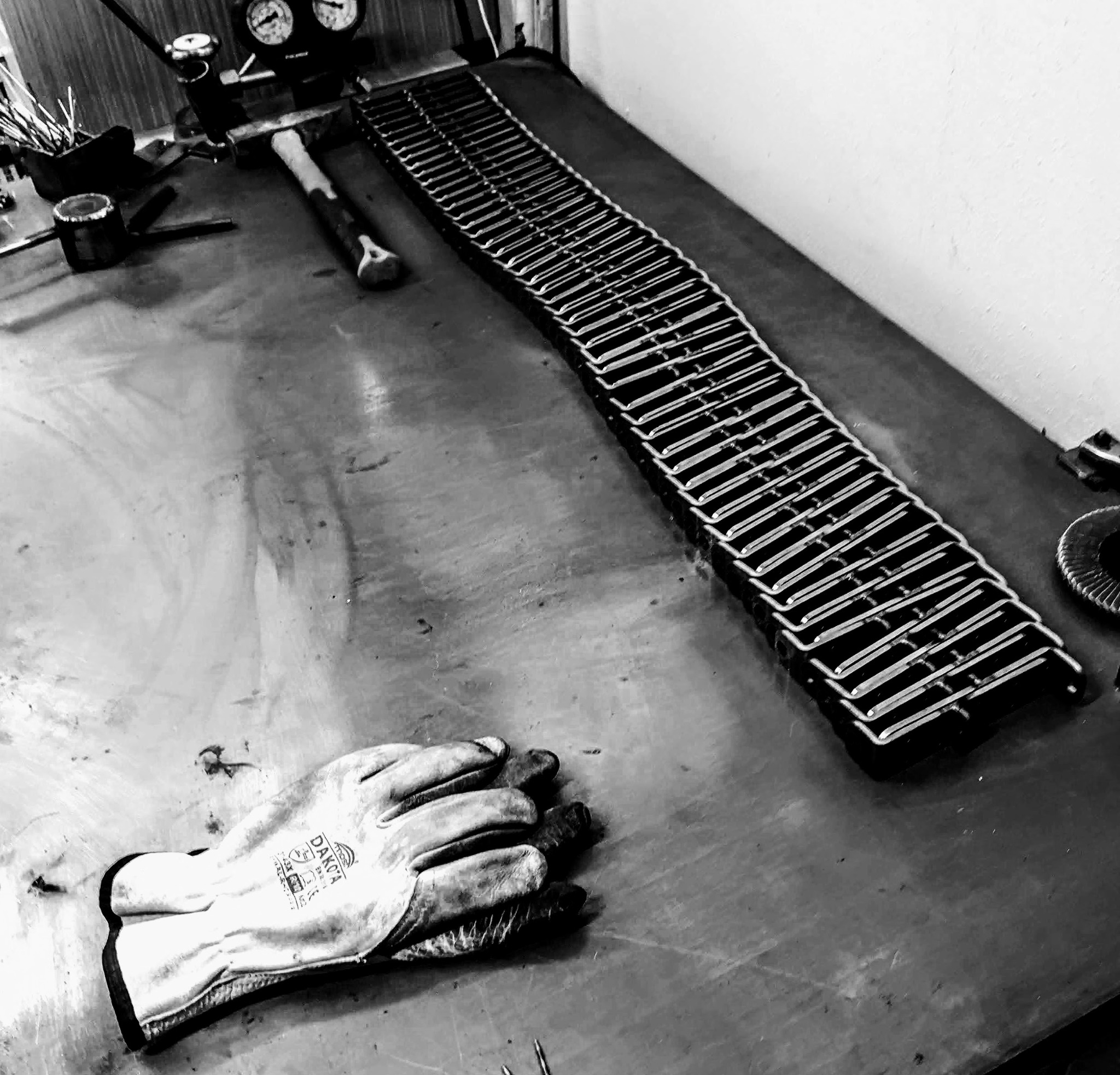 Czarno-białe zdjęcie warsztatowego stołu z narzędziami, rękawicą roboczą i długim rzędem metalowych elementów konstrukcyjnych