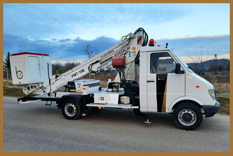 Biały podnośnik koszowy Bumar Koszalin PMT-16E, zaparkowany na asfalcie, z wysięgnikiem skierowanym w górę, widoczne logo firmy na koszu i nadwoziu.