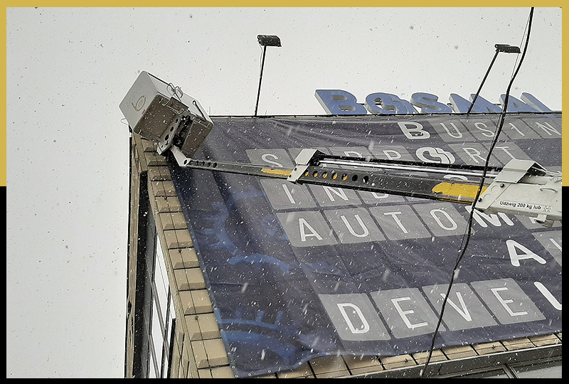 Montaż baneru reklamowego na budynku biurowym z użyciem specjalistycznego wysięgnika podczas opadów śniegu.