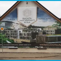 Reklama wielkoformatowa na ścianie budynku z wizualizacją apartamentów Duovita w Wiśle, z logo i hasłem 'Zainwestuj w dochodowe apartamenty'.