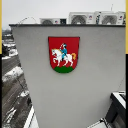 Herb miasta na elewacji budynku z klimatyzatorami na dachu, widok z góry na okolicę w zimowej scenerii.