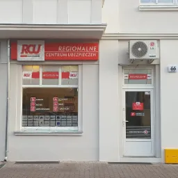 Fasada budynku z szyldem 'Regionalne Centrum Ubezpieczeń', widoczne okno z naklejkami informującymi o ubezpieczeniach firmowych, na życie, domów/mieszkań i turystycznych, oraz drzwi wejściowe...