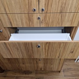 Krzysztof Mędrek - Szafa na wymiar z fornirem w odcieniach brązu, otwarta szuflada z białym wnętrzem i chromowanym uchwytem kulkowym, widoczne prowadnice szuflady.