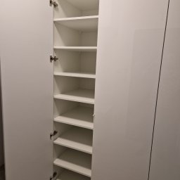 Krzysztof Mędrek - Biała szafa z otwartymi drzwiami, widoczne półki wewnątrz, minimalistyczny design.