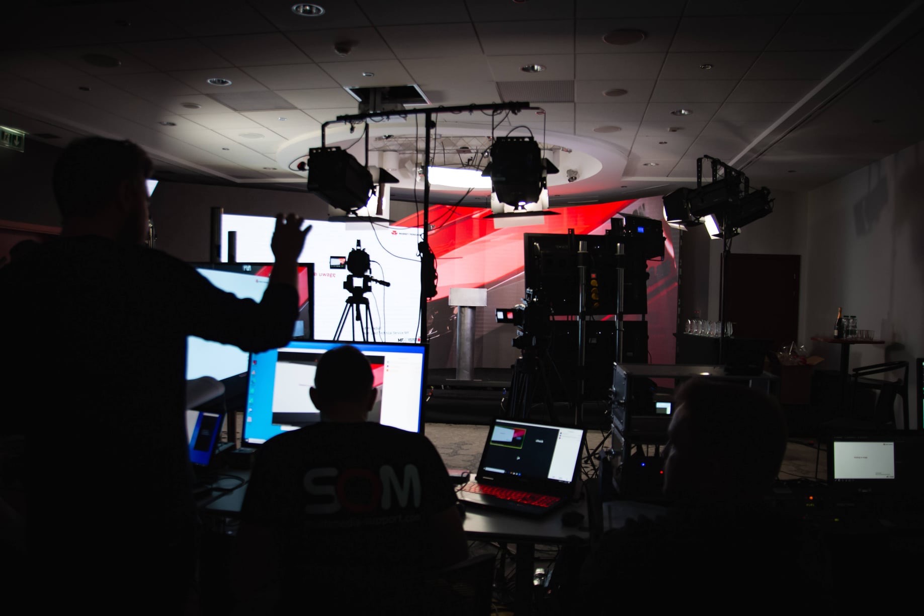 Ekipa techniczna obsługuje nagłośnienie i oświetlenie podczas wydarzenia, widoczne monitory, kamery, reflektory i konsoleta dźwiękowa.