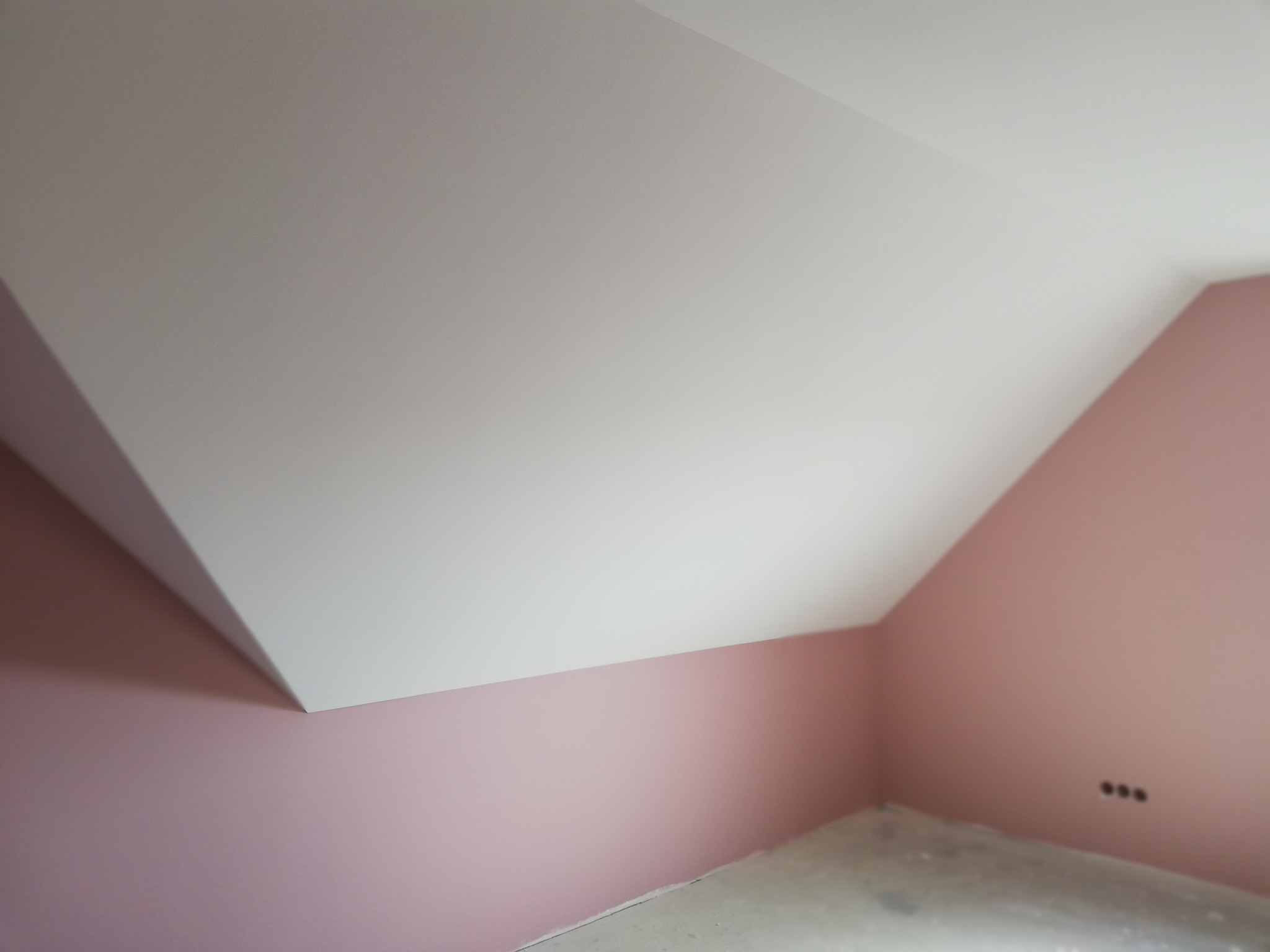 Poddasze po malowaniu ścian na różowo i wykończeniu białego sufitu, widoczne gniazdka elektryczne i surowa podłoga.