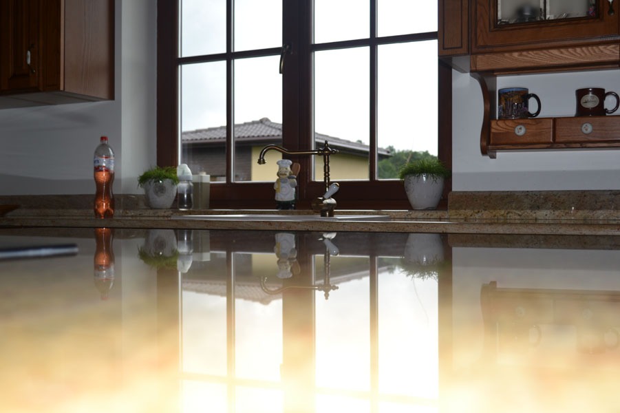Błyszczący blat w kuchni z widocznym oknem, kranem w stylu retro i dekoracjami, odbijający światło słoneczne.