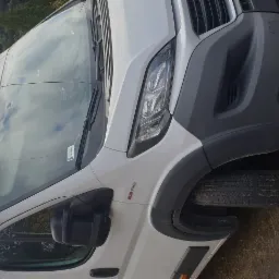 Biały bus marki Fiat Ducato 2.3 JTD zaparkowany na ziemi, widok z przodu z lekkiego ukosa.