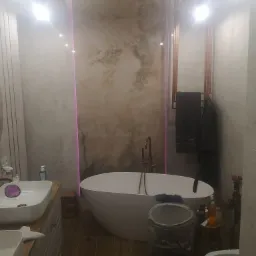 Nowoczesna łazienka z wolnostojącą wanną, umywalkami nablatowymi, podświetleniem LED i elementami dekoracyjnymi imitującymi marmur.