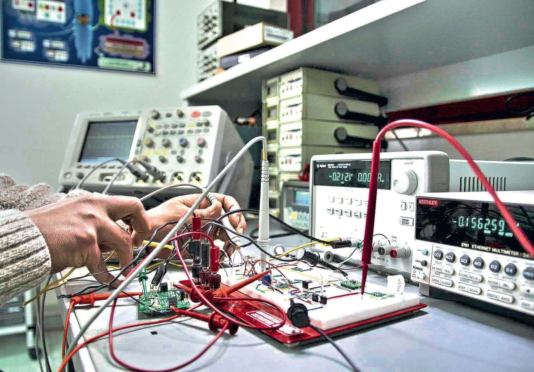 Technik w swetrze diagnozuje usterkę na płytce drukowanej za pomocą multimetru i oscyloskopu na warsztacie elektroniki.