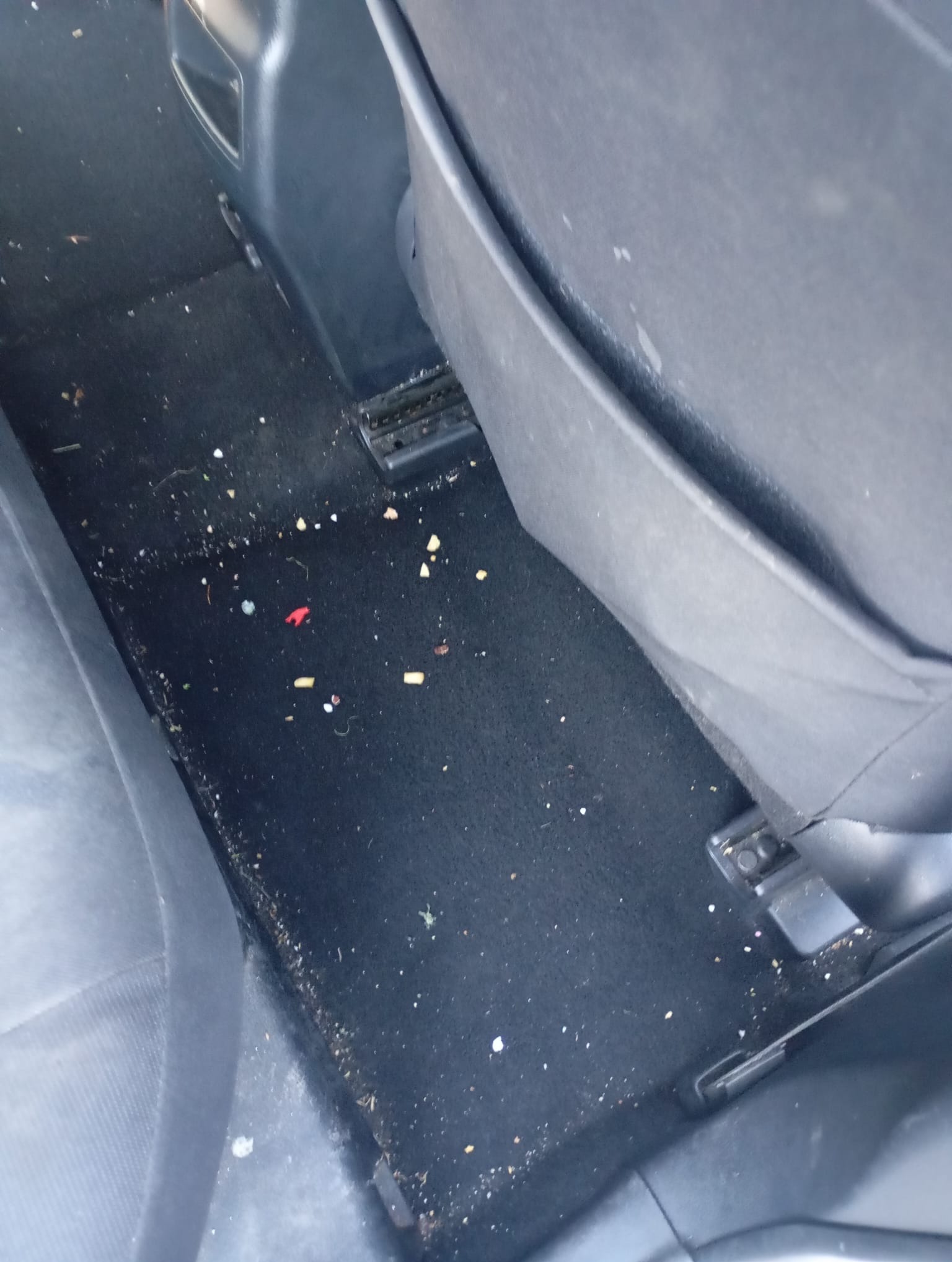 Brudna podłoga samochodu z okruchami jedzenia i kurzem, widok z góry, ciemna tapicerka, wnętrze pojazdu przed czyszczeniem.