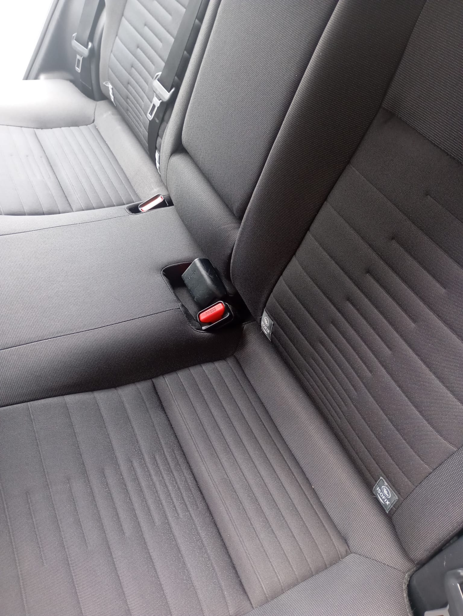 Szczegółowe ujęcie tylnej kanapy samochodowej z widocznymi pasami bezpieczeństwa, mocowaniem ISOFIX i teksturowaną tapicerką w odcieniach szarości.