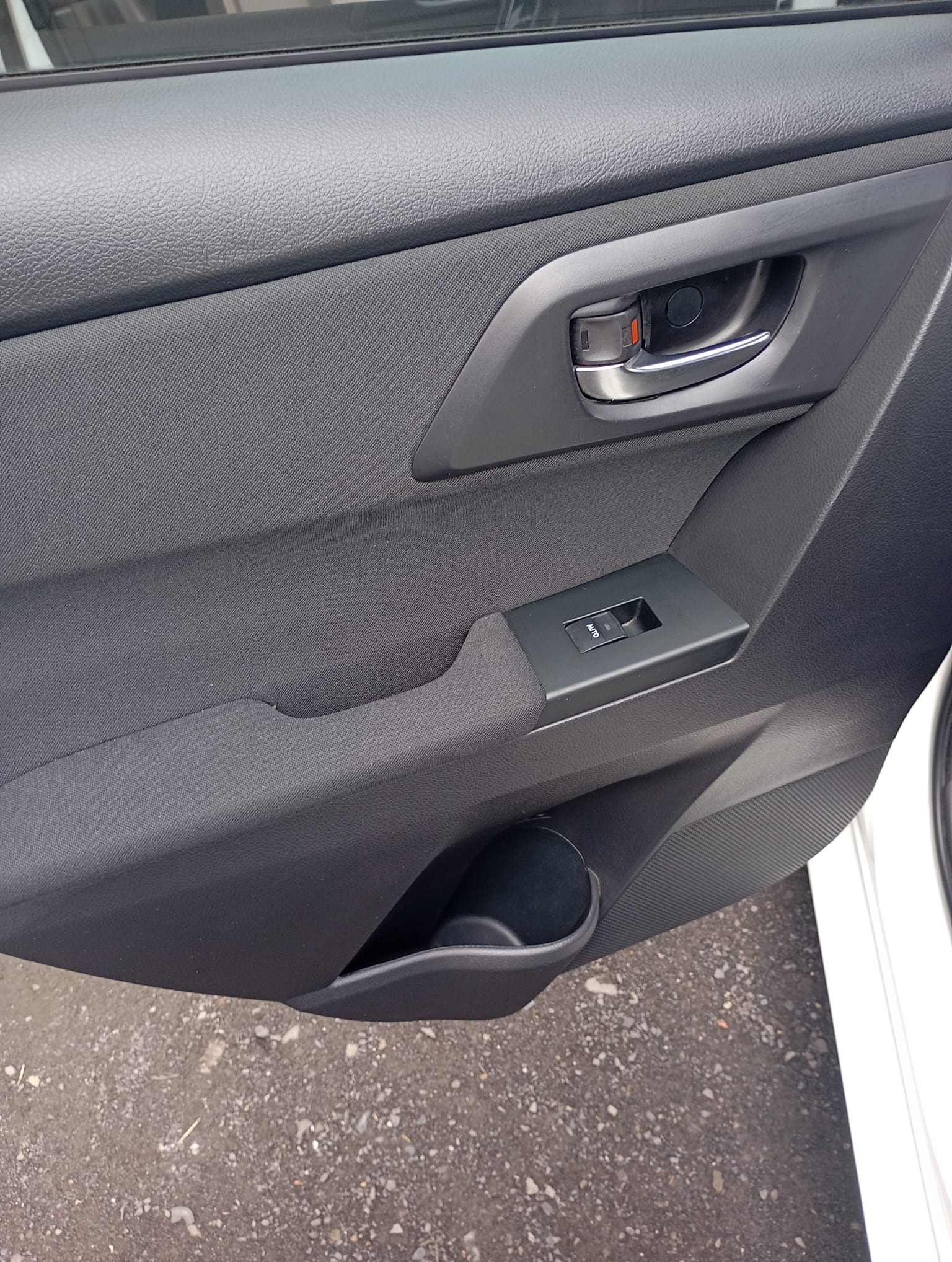 Wnętrze drzwi samochodu z czarną tapicerką, chromowaną klamką i panelem sterowania szybami. Widoczny schowek w dolnej części drzwi.