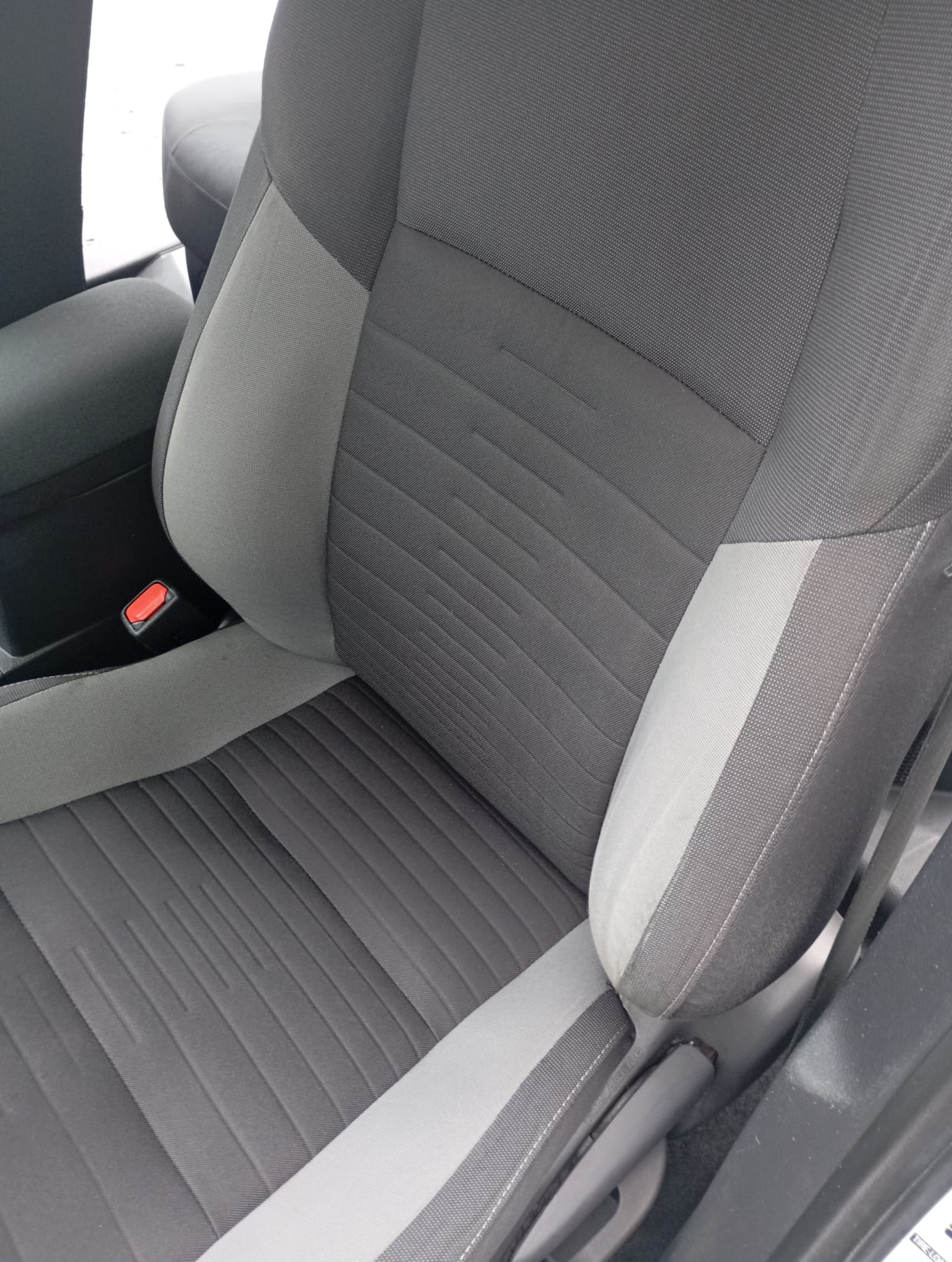 Szare, tekstylne siedzenie samochodowe z widocznym pasem bezpieczeństwa i zagłówkiem. Widoczne detale faktury materiału i przeszycia.