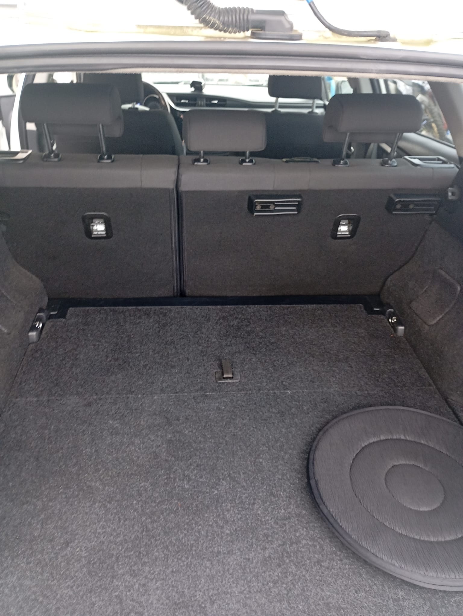 Wnętrze bagażnika samochodu z widocznym dywanikiem i tylnymi siedzeniami. Widoczny wąż odkurzacza sugeruje czyszczenie.