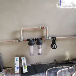 Instalacja wodna z dwoma filtrami mechanicznymi i zmiękczającymi, rury grzewcze podłogowe na podłodze, ściana w stanie surowym, widoczne opakowania filtrów Dafi.