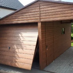 Brązowy garaż blaszany z częściowo otwartą bramą segmentową, imitujący drewno, z małym okienkiem bocznym i zadaszeniem, na kostce brukowej.