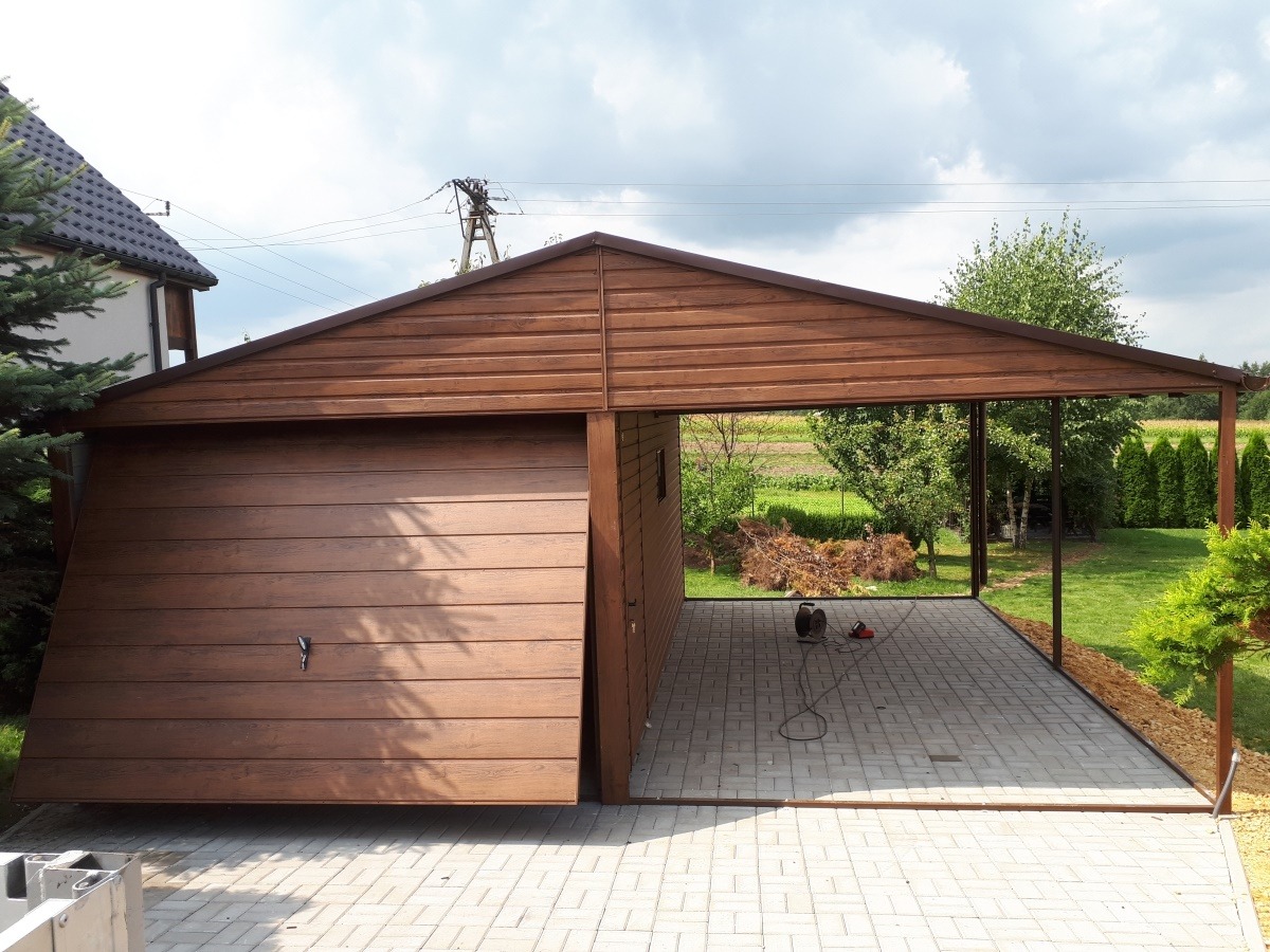 Nowoczesna, drewniana konstrukcja garażowo-wiatowa z częściowo otwartą bramą, widoczna na tle zielonego ogrodu z drzewami i krzewami, z elementami elektrycznymi na posadzce z kostki brukowej.