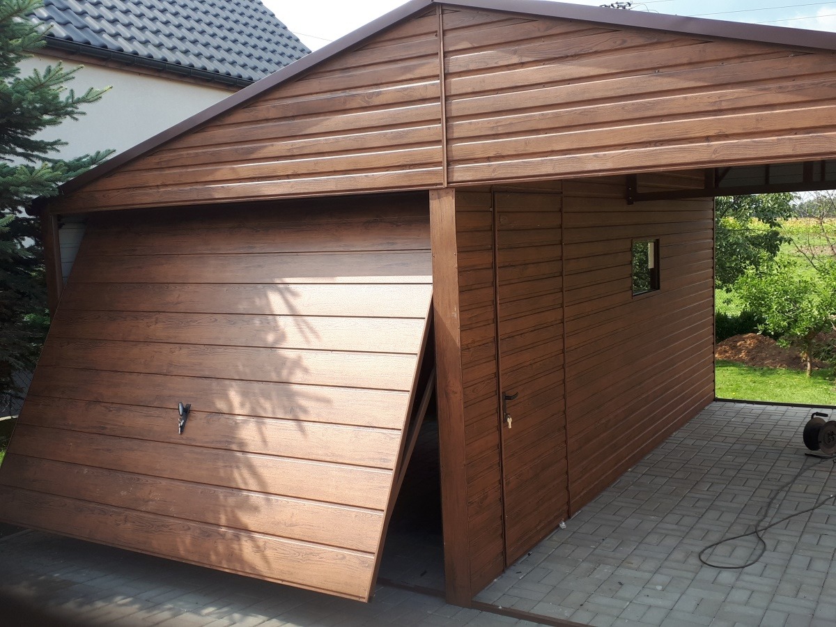 Brązowy garaż blaszany z częściowo otwartą bramą segmentową, imitujący drewno, z małym okienkiem bocznym i zadaszeniem, na kostce brukowej.