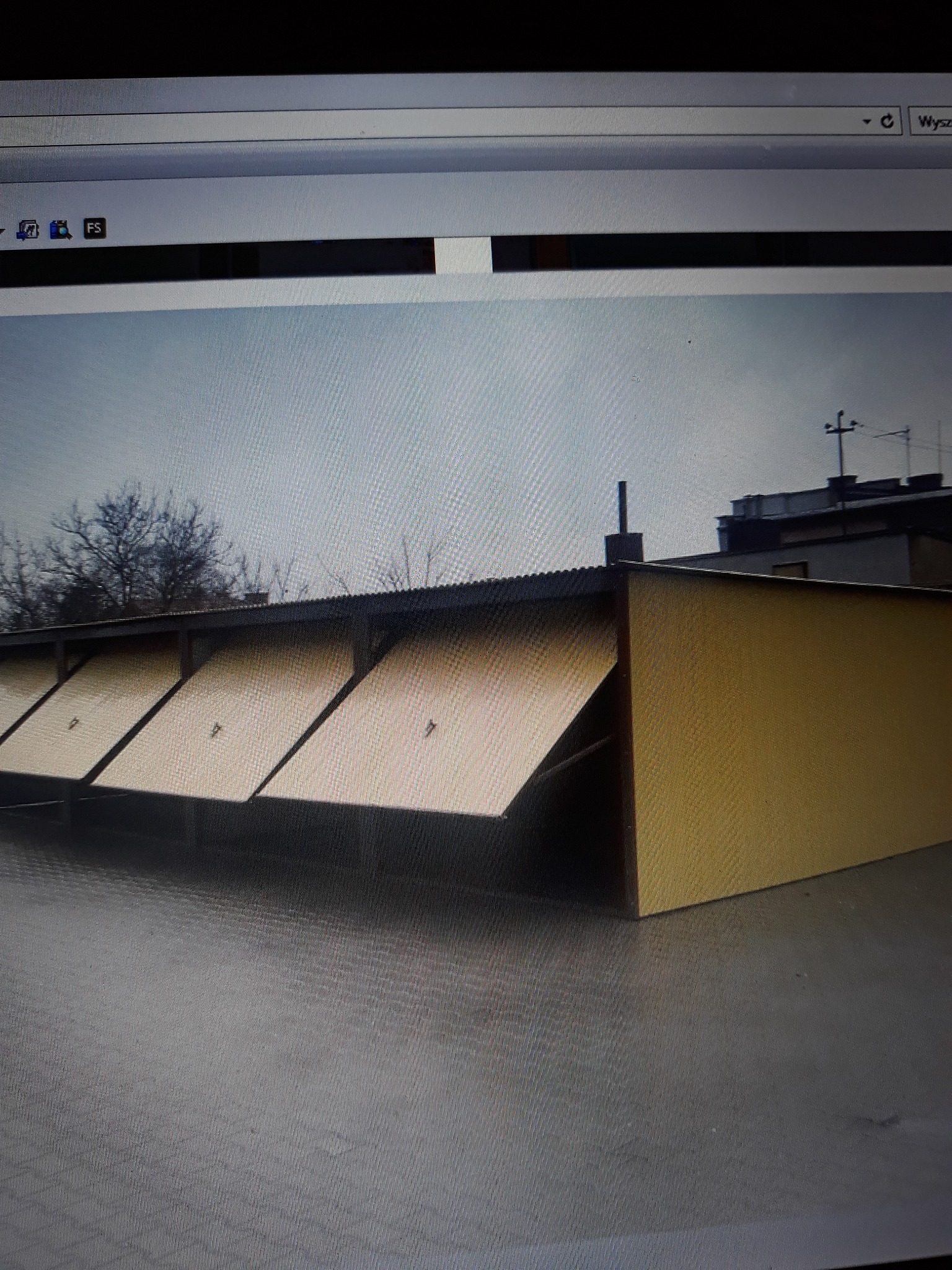 Rząd blaszanych garaży z lekko uchylonymi drzwiami w pochmurny dzień. Widoczne numery na niektórych drzwiach.