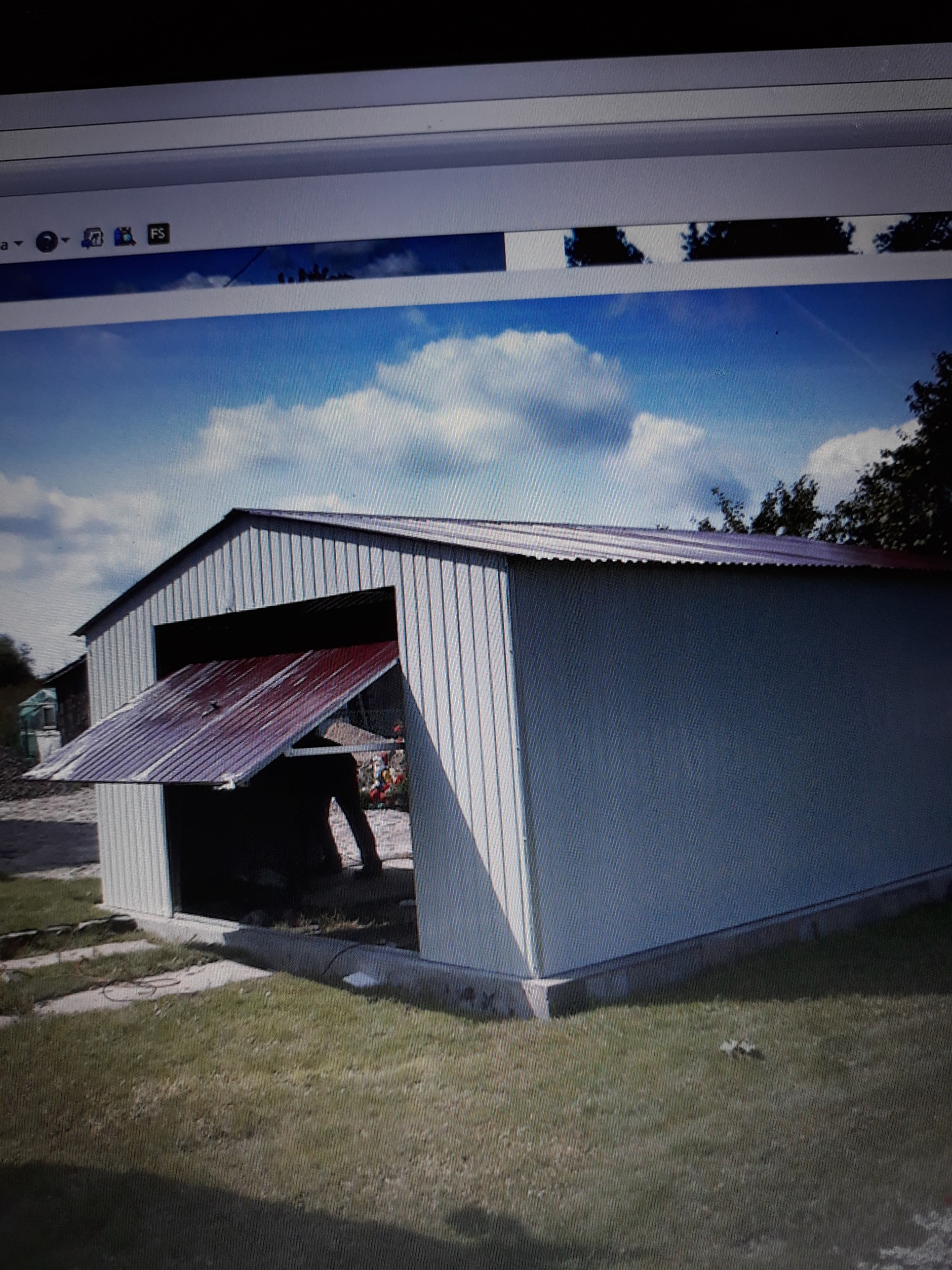 Metalowy garaż z otwartymi drzwiami w słoneczny dzień, widoczne trawnik i fragmenty nieba z chmurami.