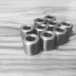 Grupka ośmiu metalowych tulejek z gwintem wewnętrznym, ułożonych na drewnianej powierzchni w czarno-białej tonacji.