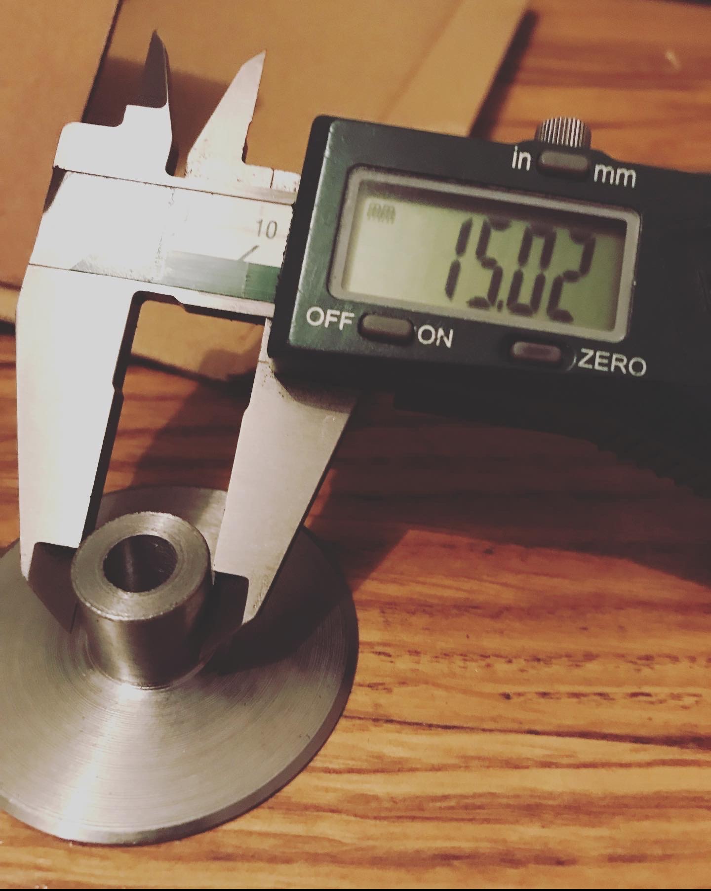 Pomiar suwmiarką cyfrową elementu metalowego o średnicy 15.02 mm na drewnianym blacie.