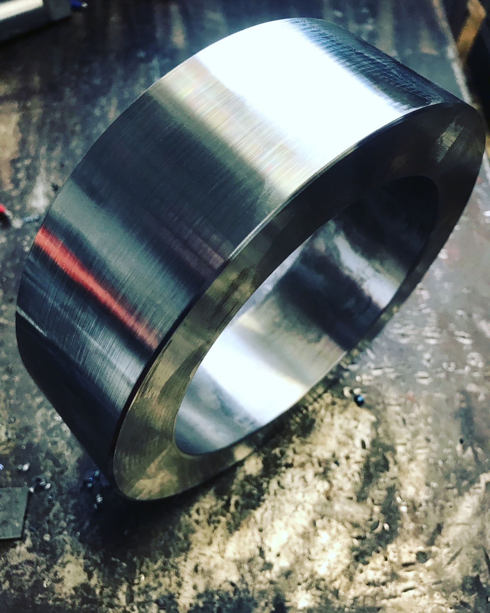Metalowy pierścień po obróbce tokarskiej, widoczne ślady obróbki na powierzchni, leżący na zabrudzonym stole warsztatowym.