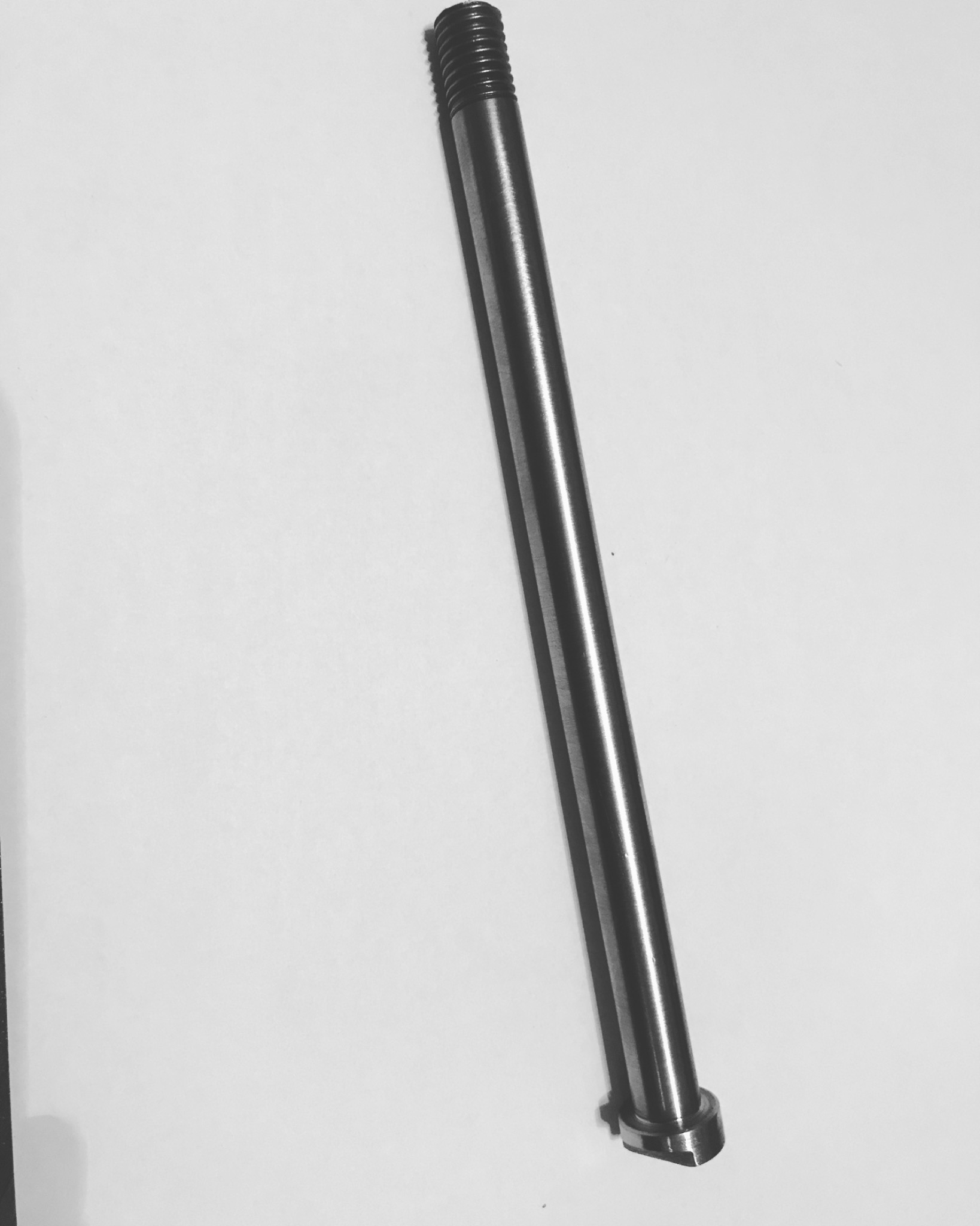 Metalowy, cylindryczny element z gwintem na jednym końcu, leżący ukośnie na białym tle, prawdopodobnie wykonany na tokarce.