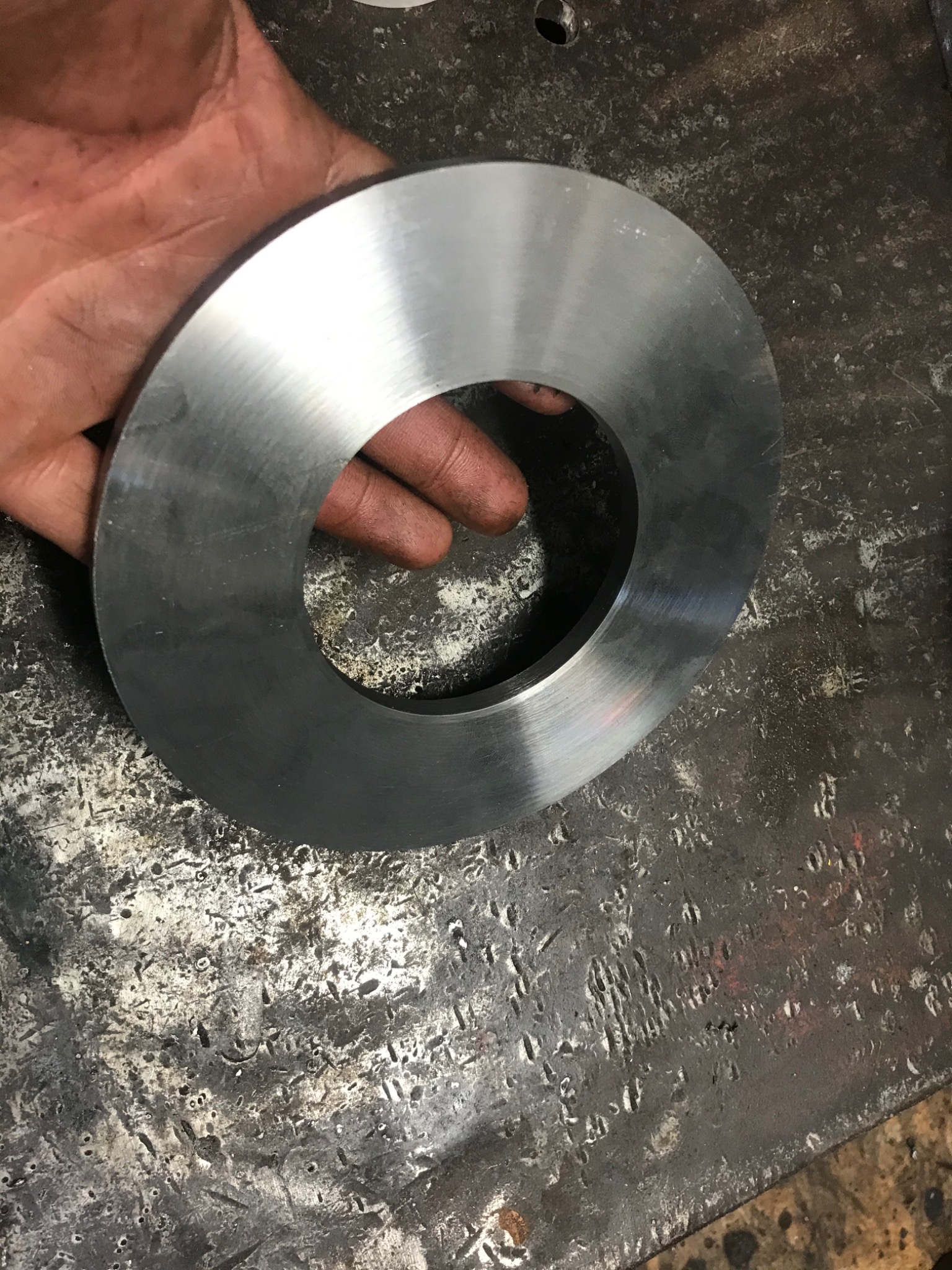 Obrabiany metalowy pierścień z otworem w dłoni na tle warsztatowego stołu z widocznymi śladami obróbki.