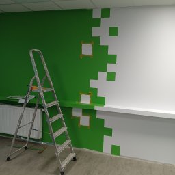 GRZEGORZ SOWIŃSKI FIRMA HANDLOWO USŁUGOWA INOWEST - Ściana w biurze w trakcie malowania na zielono i biało w pikselowy wzór, zabezpieczona taśmą malarską, drabina malarska obok, widoczny grzejnik i wiadro z farbą na podłodze.