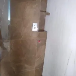 Wykończona ściana prysznicowa z brązowych płytek imitujących marmur, wbudowane półki i odpływ liniowy, biała ściana z płytek po prawej stronie.