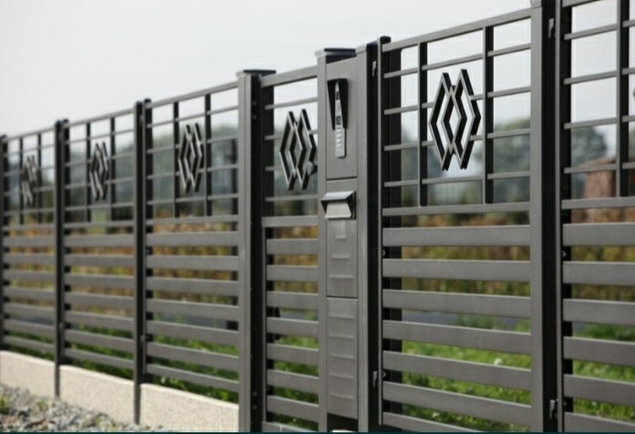 Nowoczesne ogrodzenie metalowe w kolorze grafitowym z poziomymi panelami i dekoracyjnymi elementami w kształcie rombów, zintegrowane ze skrzynką na listy i panelem domofonu.